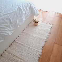 a white bed sitting on top of a hard wood floor next to a vase filled with flowers