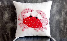 a white pillow with a red crab embroidered on the front and back, sitting on a chair