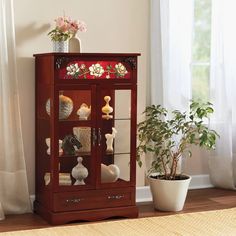 a wooden cabinet with glass doors and flowers on it next to a potted plant