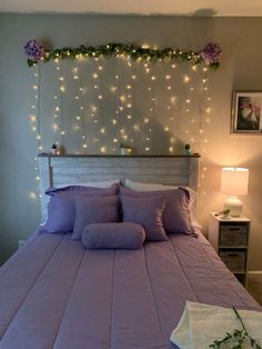 a bed that has some lights on the headboard and pillows in front of it