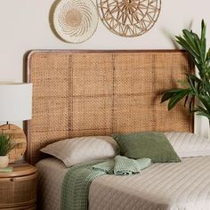 a bed with two plants on the side and a wicker headboard above it