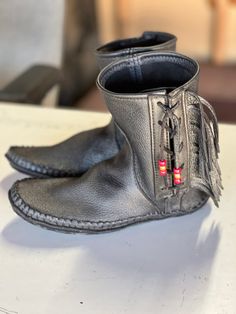 Custom handmade by me in California. These boots are side fringe side lace, made from soft, luxurious black moose. They have four soles with a copper insole for grounding to the earth. You can order any size men's, or women's with or without fringe. many colors to choose from. We offer a optional tooling leather sole. We guarantee satisfaction. Traditional Black Boots With Leather Sole, Western Style Leather Ankle Boot Moccasins, Black Leather Moto Boots For Festival, Handmade Black Boots With Round Toe, Traditional Black Leather Boots, Handmade Black Leather Boots, Black Leather Moccasins With Textured Sole, Leather Lined Slip-on Moccasins With Moc Toe, Masculine Leather-lined Moccasins With Round Toe