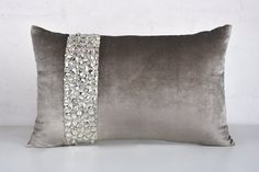 a grey pillow with silver sequins on the side and a beaded trim