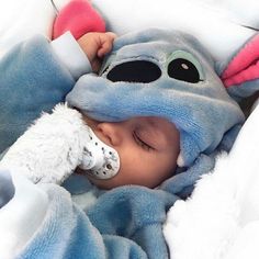 a baby wrapped in a blanket sleeping on top of a bed with a stuffed animal covering it's face