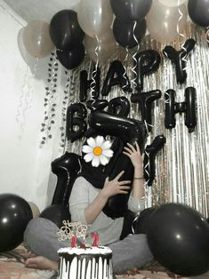 a woman sitting in front of a birthday cake with balloons and streamers around her