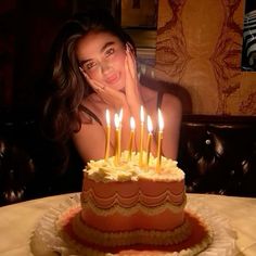 a woman sitting in front of a cake with lit candles on it and looking at the camera