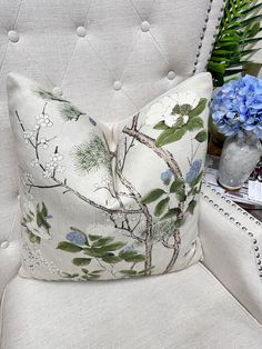 a white chair with a blue flowered pillow on top of it next to a potted plant