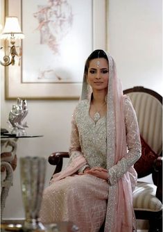 a woman sitting in a chair wearing a white dress and pink shawl on top of her head