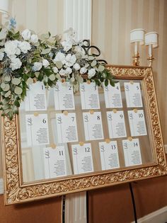 a gold framed calendar with white flowers and greenery