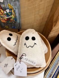 two stuffed ghost pillows sitting on top of a wooden bowl next to some pencils