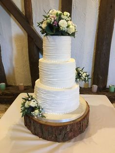 a white wedding cake sitting on top of a wooden table next to some flowers and greenery