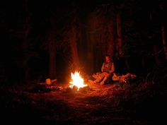 a man sitting next to a campfire in the woods