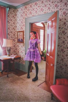 a woman in a purple dress is standing in a room with floral wallpaper on the walls