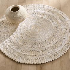 a white vase sitting on top of a wooden floor next to a large round rug