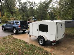 an off - road camper trailer is parked next to a blue truck in the driveway