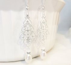 a pair of white pearl and crystal earrings on top of a table next to a vase