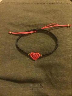 a red and black string bracelet with a heart charm on it, sitting on top of a green shirt