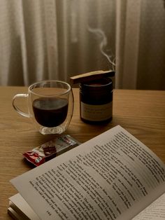 an open book sitting on top of a wooden table next to a cup of coffee