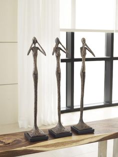 three metal sculptures are sitting on a wooden table in front of a window with white curtains