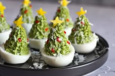 deviled eggs decorated with christmas trees are on a black plate, ready to be eaten