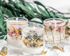 three glass candles sitting on top of a white doily next to leaves and flowers