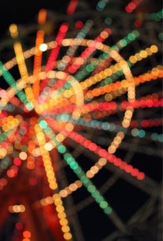 a ferris wheel is lit up at night with colorful lights in the foreground and blurry circles around it