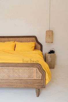 a bed with yellow sheets and pillows in a white room next to a wall lamp