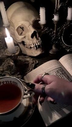 a person is holding a tea cup in front of a skull with candles on the table