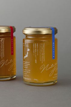 two jars of honey sit side by side on a gray surface, one has a blue ribbon around the top