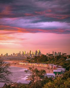 the city skyline is lit up in pink, purple and yellow as the sun sets