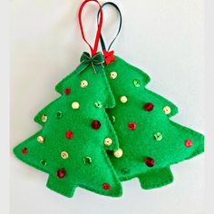 two felt christmas trees are hanging on a white wall with red and green ribbons around them