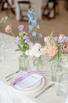 there are flowers in vases on the table with plates and napkins next to each other