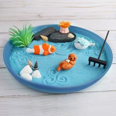 a blue plate topped with different types of toy animals and plants on top of sand