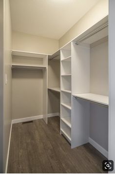 an empty walk in closet with white shelving and wood flooring on the side