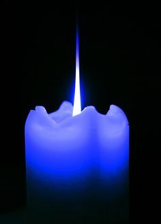 a lit candle in the dark with blue light coming from it's top and bottom