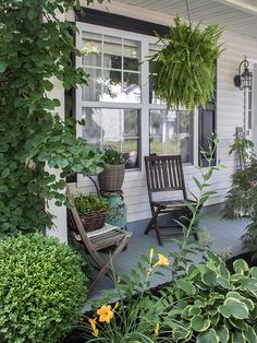 a porch with chairs and plants on the front lawn, next to a white house