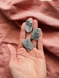 a person holding two pieces of metal with flowers on them in their palm, while the other hand holds something