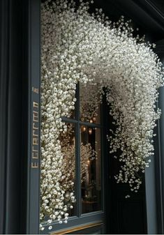 white flowers are hanging from the window of a storefront in front of a black building