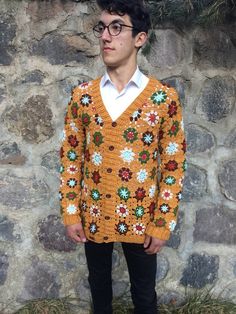 a man standing in front of a stone wall wearing a sweater with flowers on it