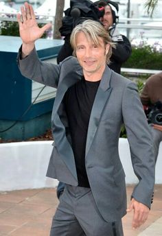 a man in a suit waves to the camera as he walks down a sidewalk with his hands up