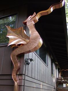 a metal dragon sculpture on the side of a house