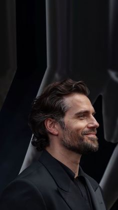 a man with long hair and beard wearing a black suit standing in front of a star wars logo