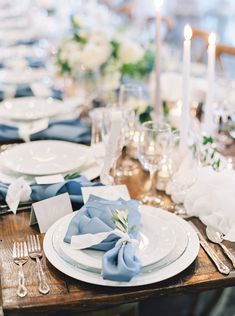 the table is set with plates, silverware and blue napkins for an elegant dinner