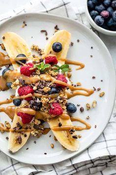 a white plate topped with bananas and blueberries next to a bowl of granola