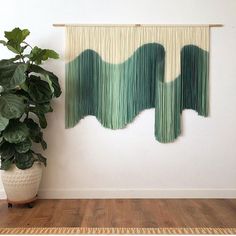 a large green plant sitting next to a white wall hanging on a wooden frame in front of a potted plant