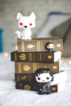 three books stacked on top of each other with two small figurines next to them