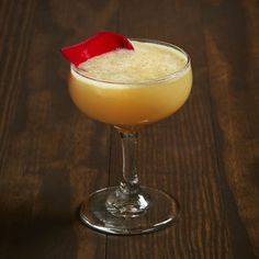 an alcoholic cocktail with a red garnish on the top sits on a wooden table