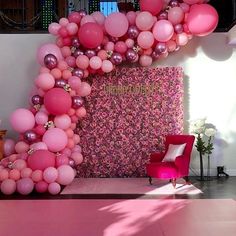 pink and purple balloons are hanging from the ceiling in front of a wall with a sign on it