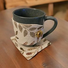 a coffee cup sitting on top of a wooden table next to a white cloth napkin