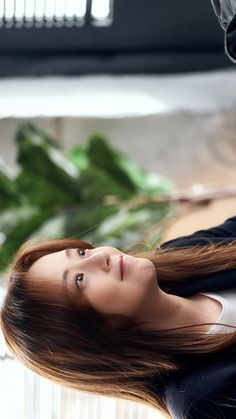 a woman with long red hair is posing for a photo in front of some plants